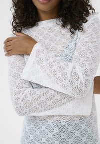 Hvid bluse i blonde med lange, klokkeformede ærmer. Fint blomsterdesign, let tekstur og en afslappet pasform. Udhullet er bådformet.