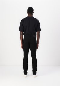 T-shirt noir en coton et jeans noirs slim, vus de dos. Les jeans ont une texture lisse et sont assortis à des baskets blanches minimalistes.