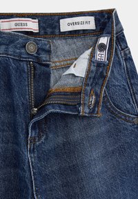 Jeans in denim di colore blu scuro con una vestibilità oversized. Presentano una chiusura a zip, bottone e cuciture arancioni lungo le cuciture e i bordi delle tasche.