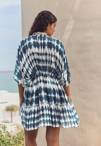 Bawełniany kaftan w kolorze morskim z białym wzorem tie-dye, z talią podkreśloną paskiem, krótkimi rękawami i luźnym krojem sięgającym nad kolano.