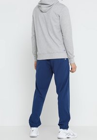 Grauer Kapuzenpulli und blaue Sporthose mit elastischen Bündchen, kombiniert mit weißen Turnschuhen. Glattes Material mit minimalen Branding-Details.