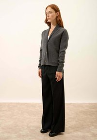 Szary wełniany kardigan z kołnierzem szalowym, zapinany na guziki, z dwoma przednimi kieszeniami. Połączony z luźnymi czarnymi spodniami i czarnym obuwiem.