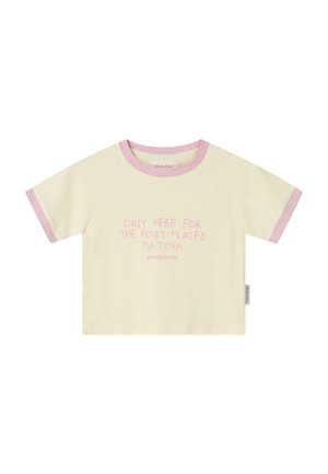 Kremowy t-shirt z krótkim rękawem, wykończony różowym obszyciem i różowym napisem z przodu: "Tylko tutaj dla matchy po Pilatesie", metka na bocznym szwie.