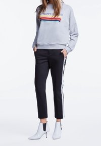 Sudadera gris con texto y rayas de arcoíris, combinada con pantalones negros recortados con rayas laterales blancas y botas de tobillo blancas.