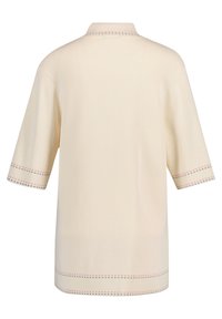 Krémový pulovr s krátkým rukávem. Tkaná textura s kontrastním dekoračním stehem v červené a černé barvě kolem límce a rukávů.