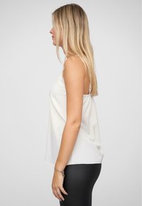 Witte mouwloze top met kantdetails op de halslijn, zachte stof, losse pasvorm en rechte zoom, gedragen over zwarte legging.