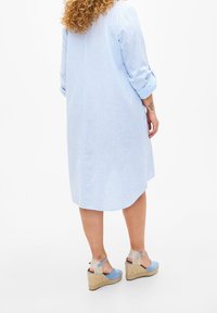 Helles blaues, gestreiftes Hemdkleid mit Dreiviertelärmeln, abgerundetem Saum und subtiler Textur; kombiniert mit Wedgesandalen in hellblau und beige.