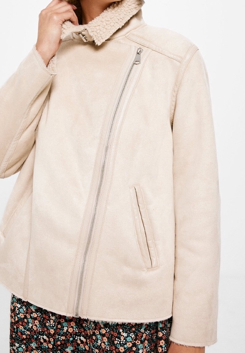 Beige jack van nep-shearling met een ritssluiting, kraag en een gladde textuur, met een licht getailleerde pasvorm en strakke lijnen.