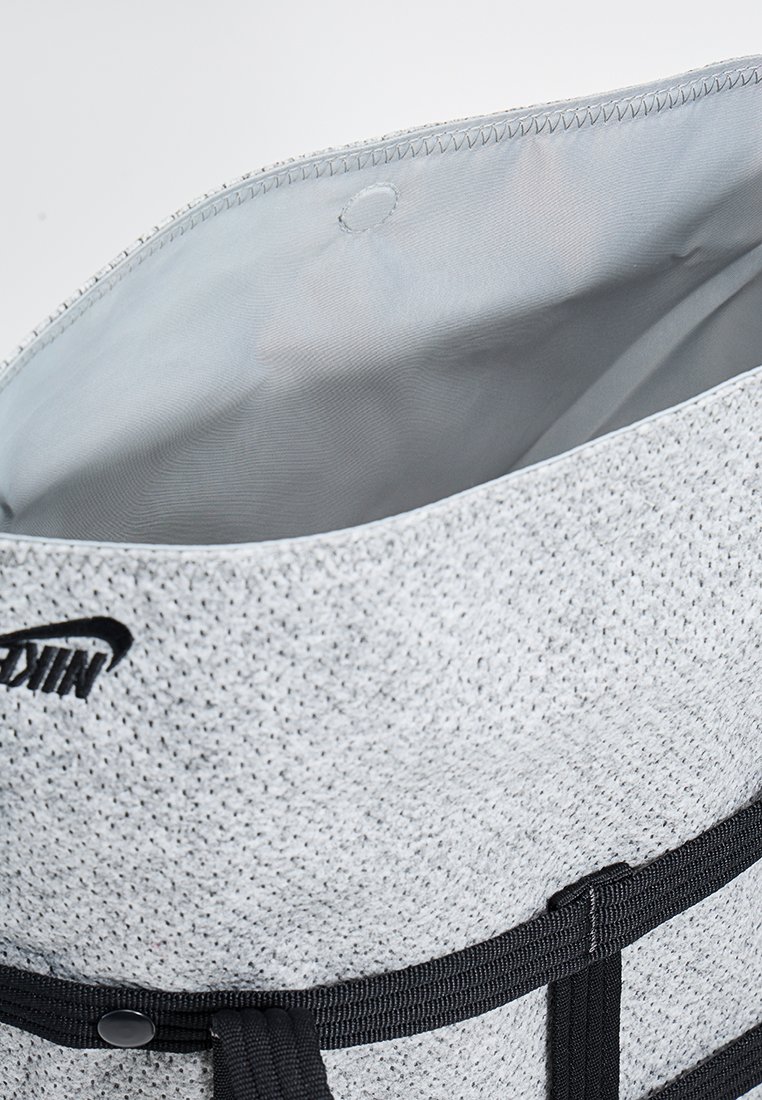 Grau textile Tragetasche mit gemustertem Äußeren, schwarzen Trägern, schwarzem Logo und glattem, hellfarbigem Innenfutter.