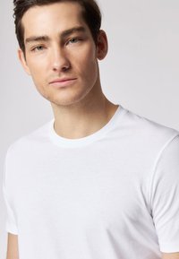 Maglietta bianca in cotone con scollo rotondo, maniche corte e una texture liscia. Design semplice senza motivi o grafiche visibili.