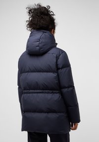 Marine blauwe pufferjack met een strakke capuchon, voorzien van een gequilte uitstraling en een elastische taille voor een betere pasvorm. Glad, waterafstotend materiaal.