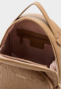 Zaino in pelle tan con marchio inciso, zip dorata e spazioso interno con tasca zip e morbida fodera rosa.
