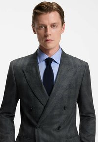 Completo grigio a doppio petto con una texture sottile, abbinato a una camicia dress leggera blu chiaro e una cravatta blu navy, con bottoni neri e vestibilità su misura.