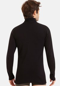Chemise noire à manches longues et col roulé présentant une texture lisse, un design ajusté et un col haut, vue de derrière.