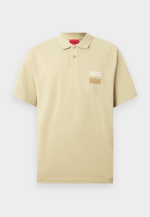 Beige polo shirt met korte mouwen, voorzien van twee knopen en een klein vierkant logo-label met de tekst "HUGO" op de linkerkant van de borst.
