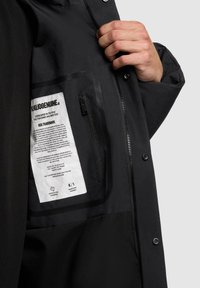 Interior de chaqueta negra con un bolsillo con cremallera y una etiqueta con instrucciones de cuidado. Textura de tela suave y diseño minimalista.