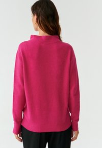 Fuchsia Pullover mit hohem Kragen und langen Ärmeln, mit weichem Material und geripptem Saum, von hinten betrachtet.