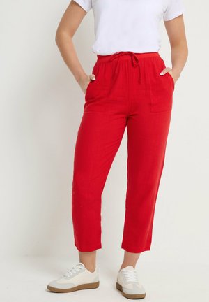 Person iført klare røde, kortere bukser med snøre i taljen og lappelommer, kombineret med hvide sneakers og en hvid t-shirt.