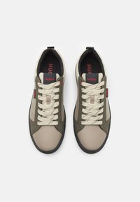 Lace-up sneakers featuring a beige and olive green leather exterior, cream laces, black sole, and a prominent red logo detail.