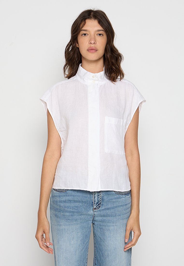 Weißes Leinen-Hemd ohne Ärmel mit hohem Kragen, Knopfverschluss vorne und einer einzelnen Brusttasche. Weicher, leichtgewichtiger Stoff mit entspannter Passform.