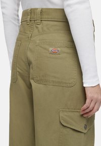 Olijfgroene werkbroek met meerdere zakken, knopenaccenten en een opgenaaide Dickies-logo patch op de achterzak. Gemaakt van duurzame stof.