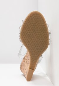 Hopeasandaalit, joissa on korkkiwedget ja kuvioitu kumipohja, jossa on kuvioitu pito, sekä koristeellisia yksityiskohtia remmeissä.