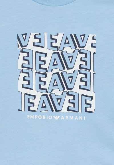 Μπλε πουκάμισο με λευκό τετράγωνο σχέδιο που περιλαμβάνει επαναλαμβανόμενα, καθρεφτισμένα γράμματα "EA" σε σκούρο μπλε, και κείμενο "EMPORIO ARMANI" κάτω από το τετράγωνο.