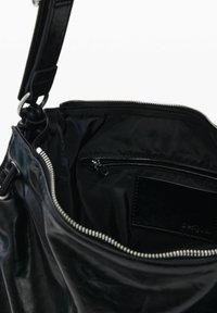 Must nahast koti sisemus, millel on lukuga tasku ja sile tekstuur. Omadusteks on hõbedane lukk ja pealmine sulgur, minimalistlik disain.