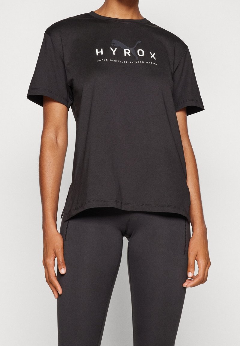 Camiseta atlética negra de manga corta hecha de un tejido ligero con cuello redondo, que presenta un logo blanco de HYROX en el pecho.