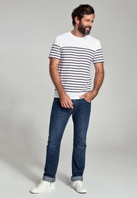 Hvid og marineblå stribet kortærmet t-shirt parret med mørkeblå jeans og hvide sneakers. Casual pasform, blød tekstur og opkrøllede ærmer.