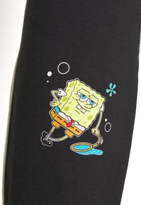 Bob l'éponge avec une expression sceptique, portant un pantalon marron et une cravate rouge, tenant une raquette bleue avec des bulles autour, sur un tissu noir.