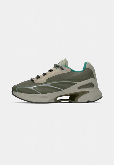 Zapatillas deportivas en verde olivo y beige con forro en azul petróleo, cordones grises y una suela gruesa acolchada con un detalle recortado cerca del talón.