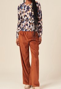 Pitkähihaista kukkakuvioista neulepuseroa valkoisena, sinisenä ja oranssina; yhdistetty tulipunaisiin corduroy-matskuihin, joissa on leveä lahje. Kankaan pinta on teksturoitu ja malli on rento.