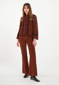 Ensemble deux pièces à motifs rouges comprenant une veste courte avec des accents marine et un pantalon évasé. Le tissu présente une texture et des détails distinctifs.