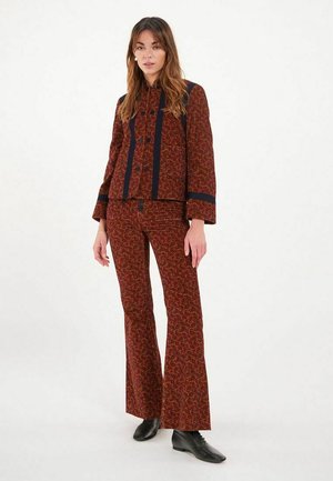 Ensemble deux pièces à motifs rouges comprenant une veste courte avec des accents marine et un pantalon évasé. Le tissu présente une texture et des détails distinctifs.