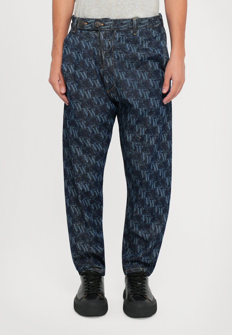 Pantaloni din denim închis, cu un model repetat de logo-uri în nuanțe de albastru, cu o croială lejeră și buzunare frontale. Se poartă pantofi negri cu șireturi.