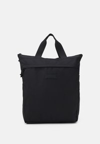 Sac tote en nylon noir avec double poignée et fermeture éclair. Présente une surface texturée et un écusson logo brodé sur le devant.