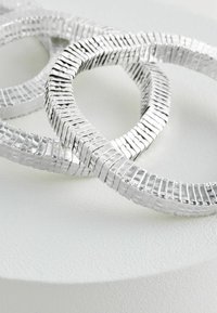 Sølv metalhoops med et struktureret, ribbet mønster. Overfladen er blank og reflekterende, hvilket fremhæver det intrikate design.