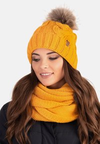 Bright yellow knit beanie with a textured pattern and a fur pom-pom on top, paired with a matching knit scarf in a similar shade.