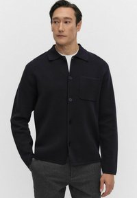 Marinblå skjorta med knappar i texturerad tyg, utrustad med spridd krage, ficka på bröstet och rak fåll för en avslappnad passform.