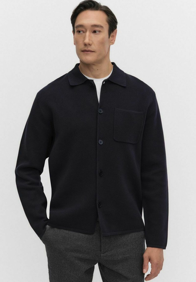 Marinblå skjorta med knappar i texturerad tyg, utrustad med spridd krage, ficka på bröstet och rak fåll för en avslappnad passform.