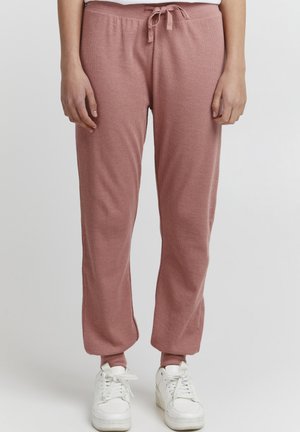 Rosa, ribbede joggebukser med snøring i livet og tapered ben, kombinert med hvite sneakers. Myk, lett stoff.