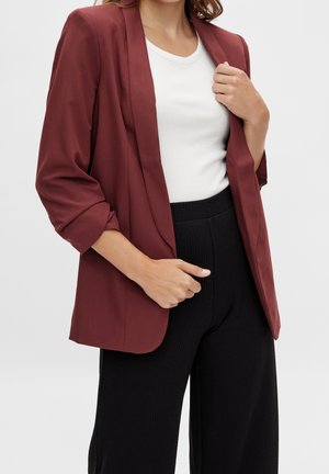 Blazer bourgogne à coupe décontractée, avec un col à revers et des manches retroussées, associé à un haut blanc à côtes ajusté et un pantalon noir.