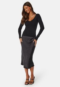 Zwarte geribbelde top met lange mouwen en een diepe V-hals, gecombineerd met een soepele donkere rok met een subtiele drape en hoge split.