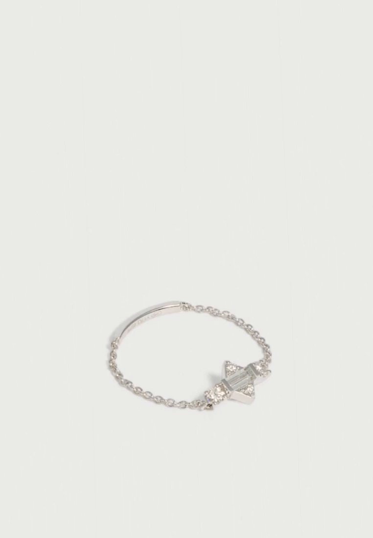 Bracelet chaîne argenté avec un élément central géométrique en forme de nœud et de petites pierres scintillantes sur un fond uni clair.