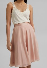 Ljusbeige linne med spetskant, kombinerad med en flödande, knälång blekrosa kjol med slät textur och bred midjeband.