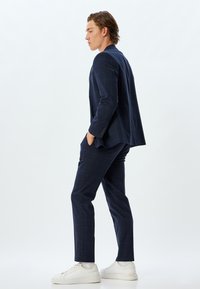 Marineblauw geblokt pak met op maat gemaakte blazer en slanke broek. Gecombineerd met witte sneakers. Soepele textuur, modern ontwerp.