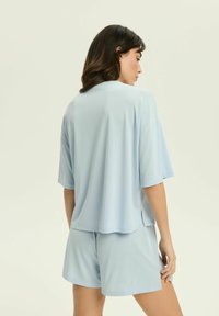 Jasnoniebieska bluzka z krótkim rękawem i dopasowane szorty z miękkiego, gładkiego materiału. Luźny krój z bocznymi rozcięciami dla dodatkowego komfortu.