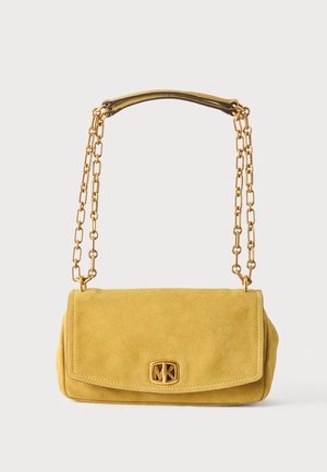 Keltainen mokkanahkainen käsilaukku, jossa kultainen ketjuhihna ja kullanvärinen Michael Kors -logo etutaskun läpän sulkemisessa valkoisella taustalla.