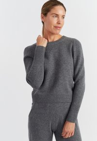 Pullover grigio in lana con collo a giro, polsini e orlo a coste; texture morbida e stile aderente, abbinato a pantaloni grigio coordinati.